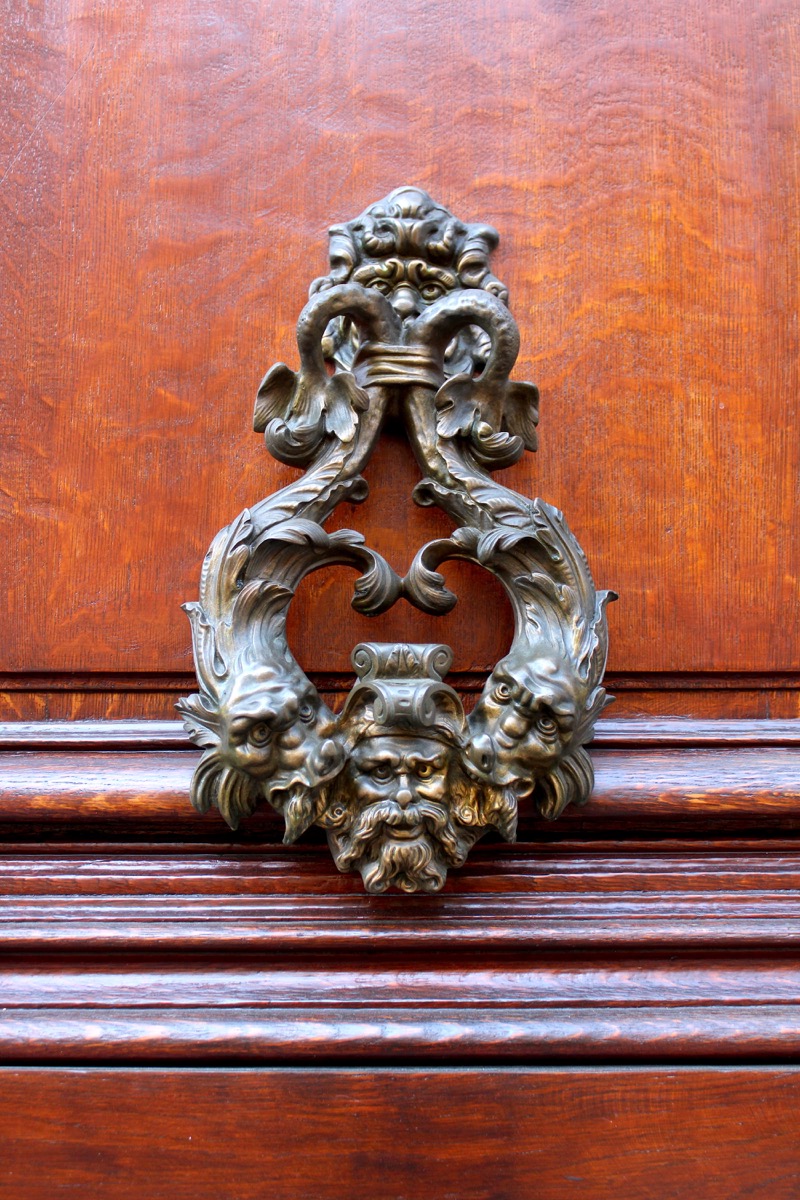 Ornate door knocker with swans and faces on a wooden door